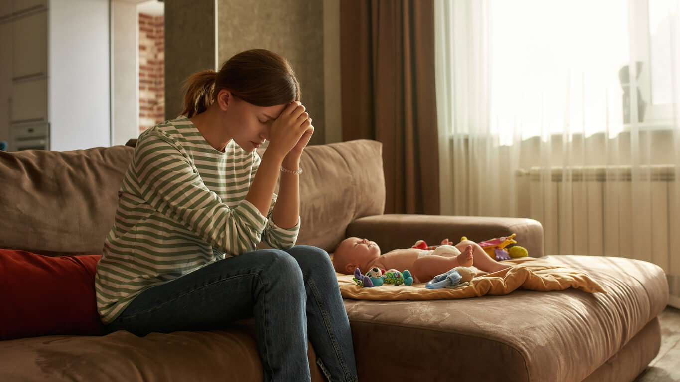 mama deprimida preocupada desolada junto a bebe solo en el sofa sillon