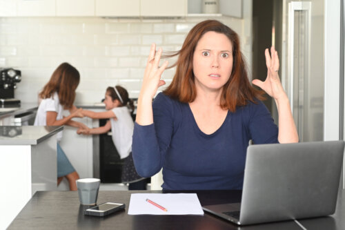 madre nerviosa en la cocina intenta hacer home office mientras hijas pelean detras