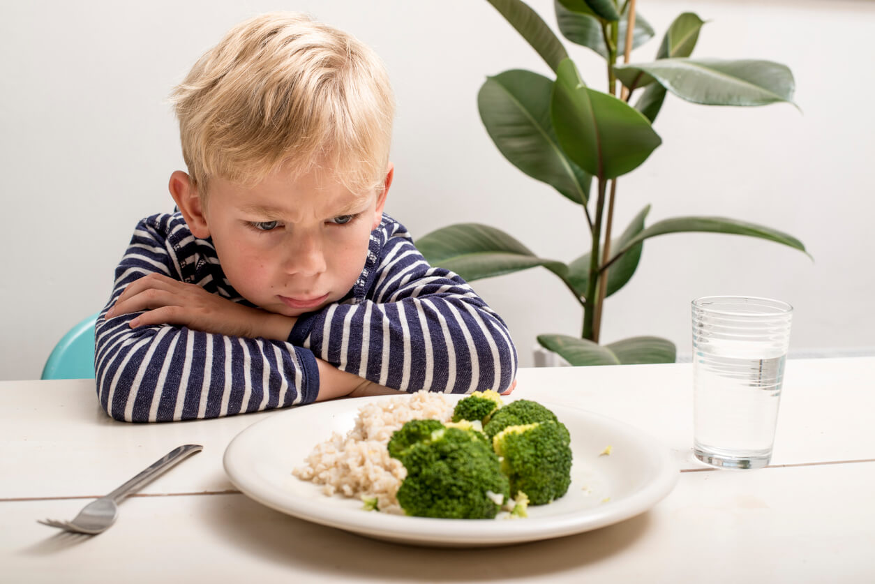 Un enfant assis devant une assiette de brocoli et de chou-fleur.