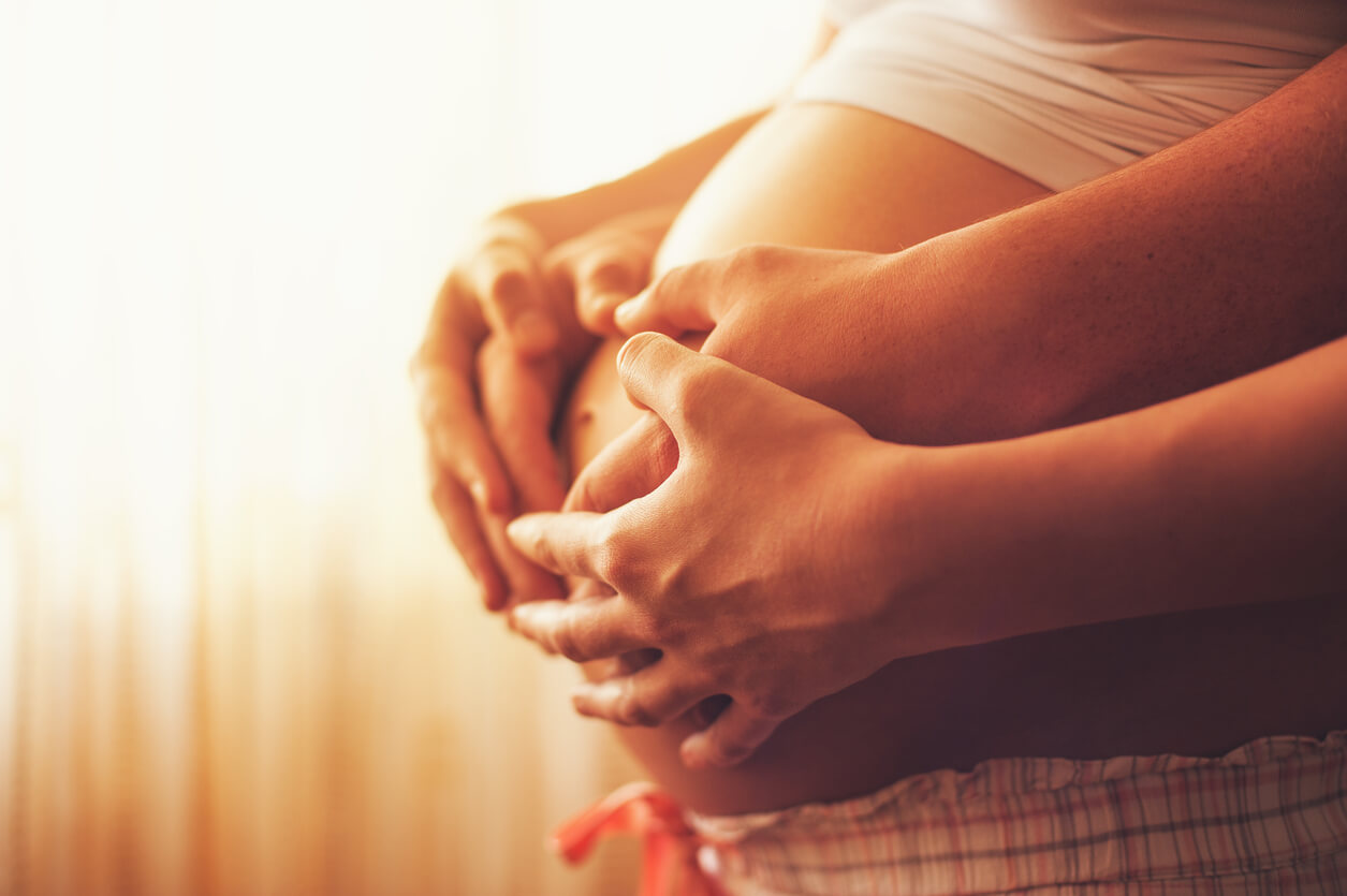Les quatre mains des parents sur le ventre de la femme enceinte.