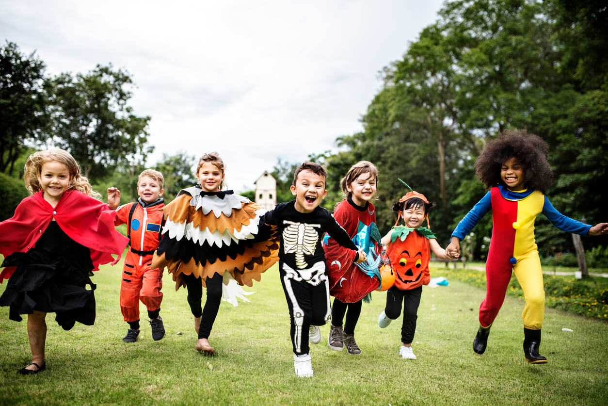 Crianças correndo no parque com fantasias de Halloween.