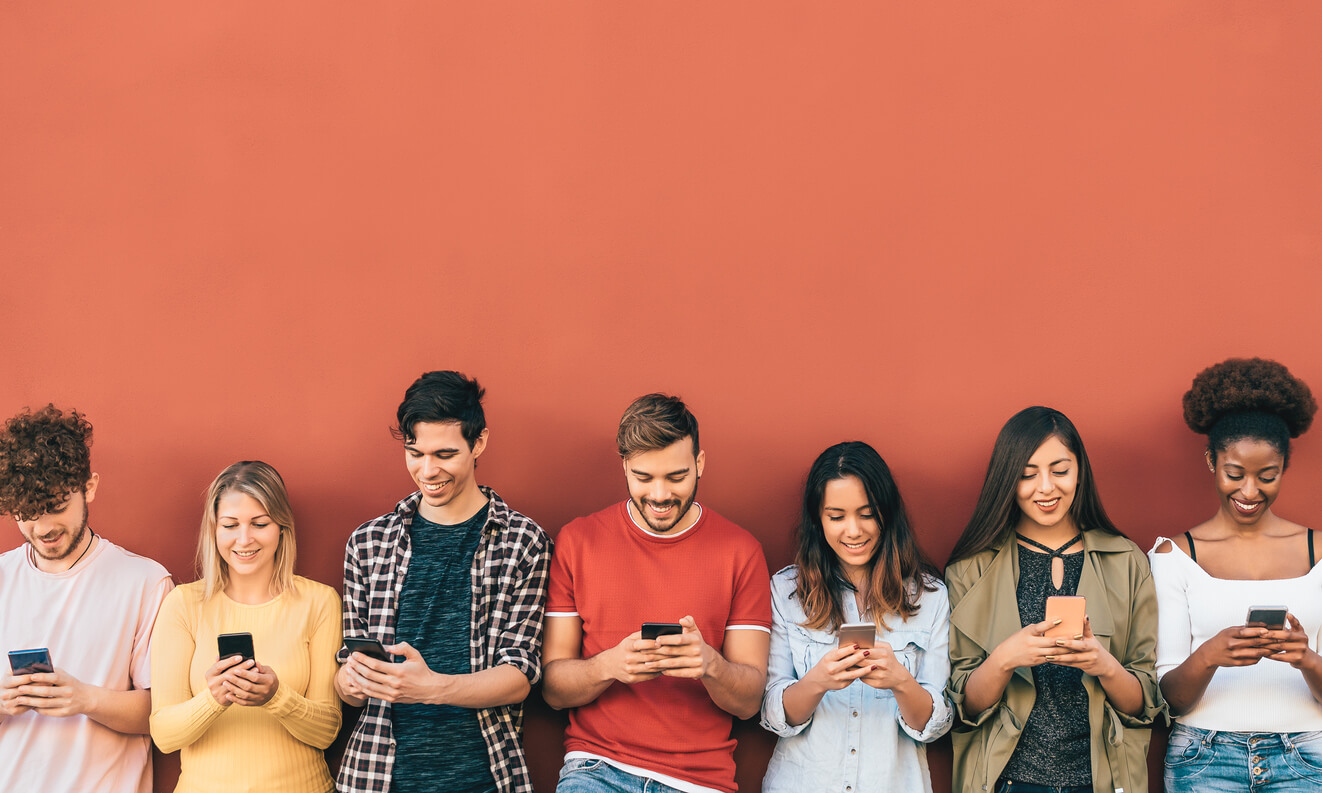 A row of teens leaning against the wall using their smartphones.