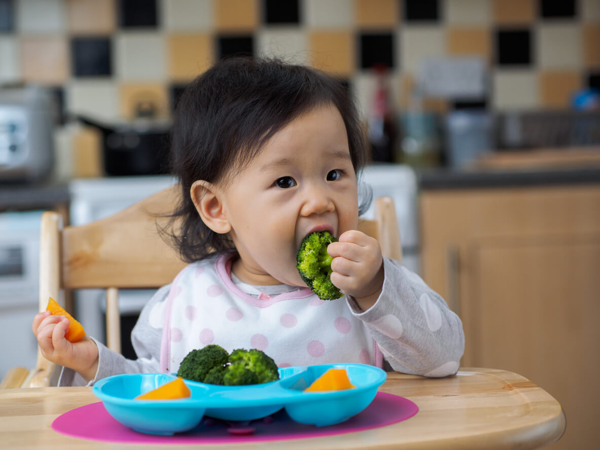 Ett litet barn som äter ångkokt broccoli och morötter.