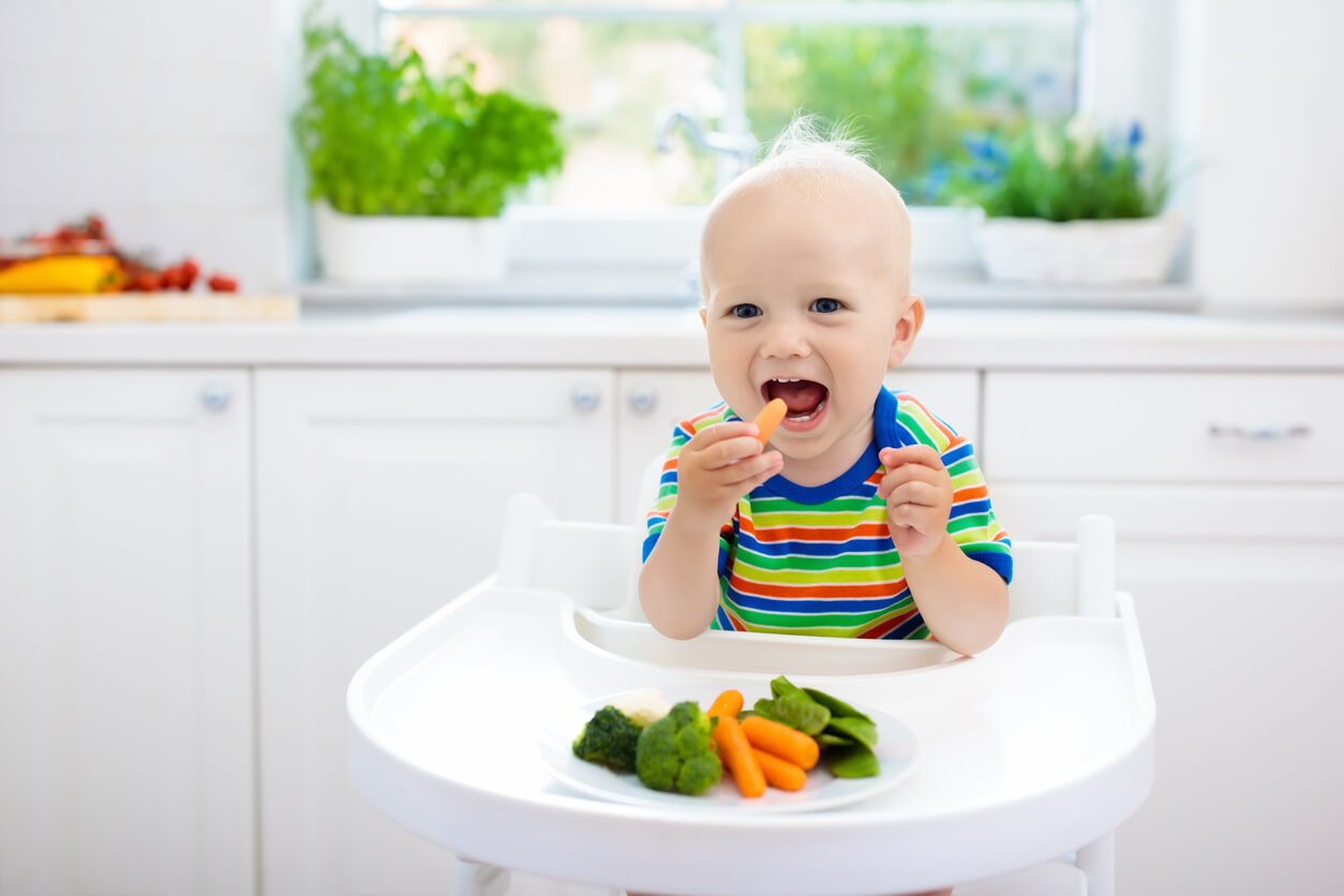 Bebê no cadeirão comendo legumes em pedaços.