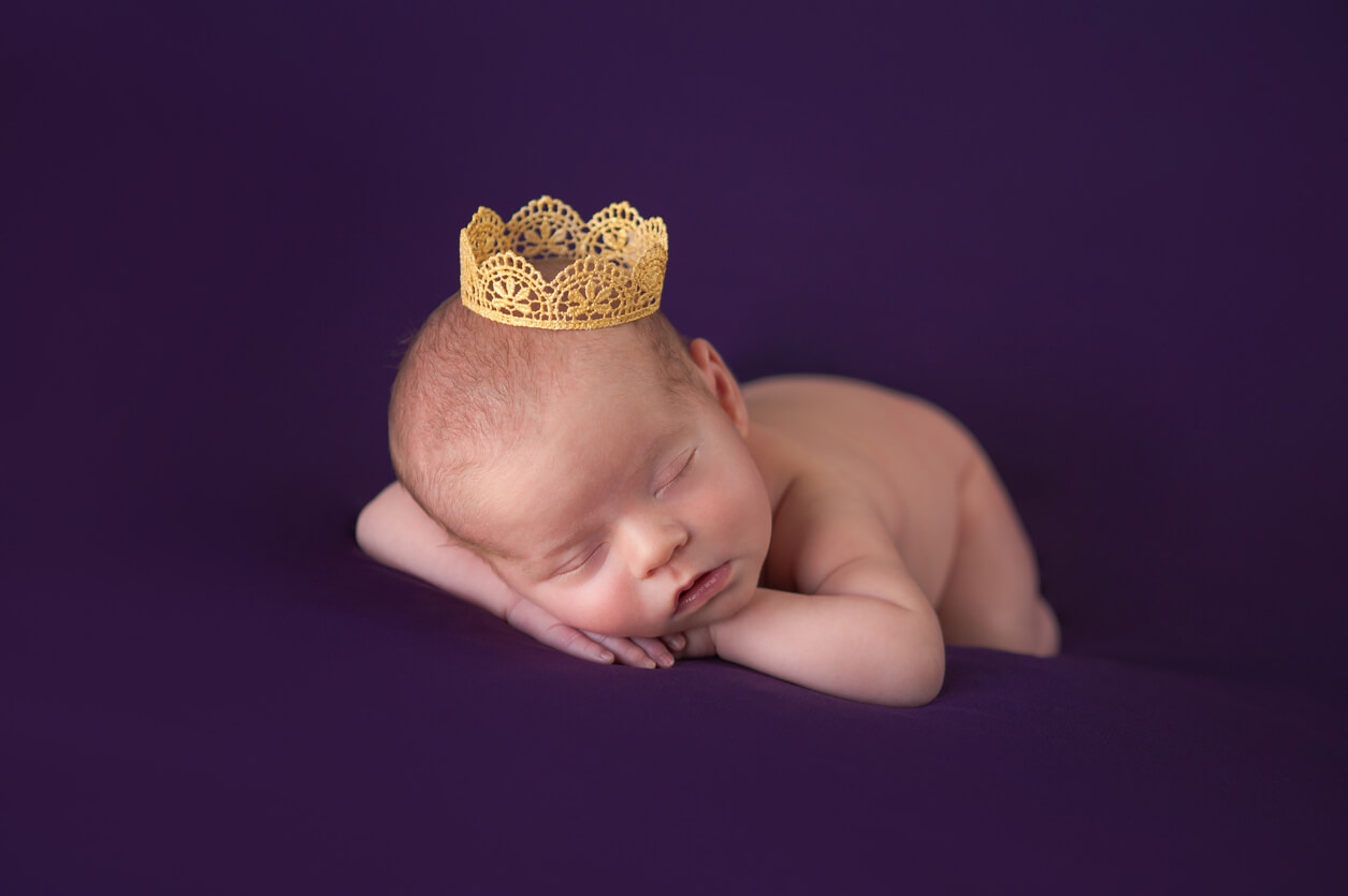 A newborn baby wearing a tiny golden crown.