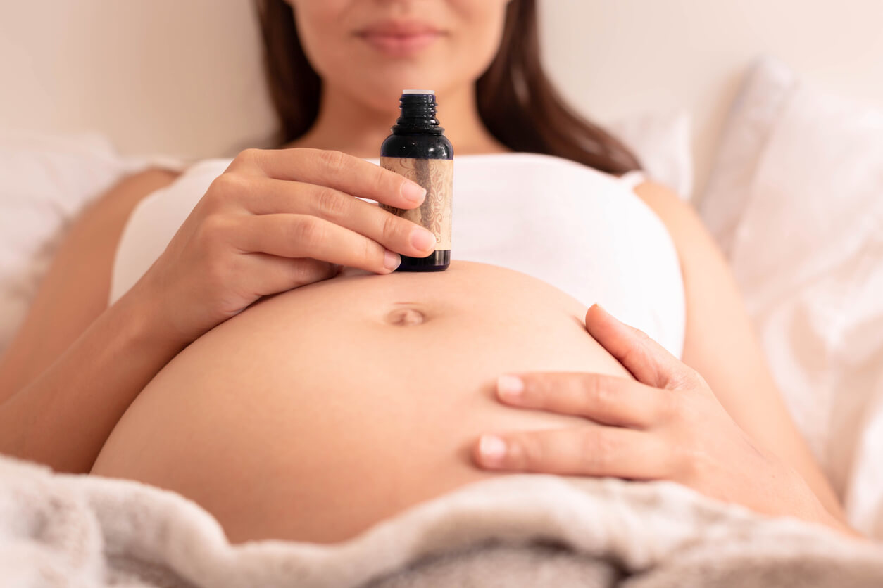 Une femme enceinte avec un flacon d'huile sur son ventre.