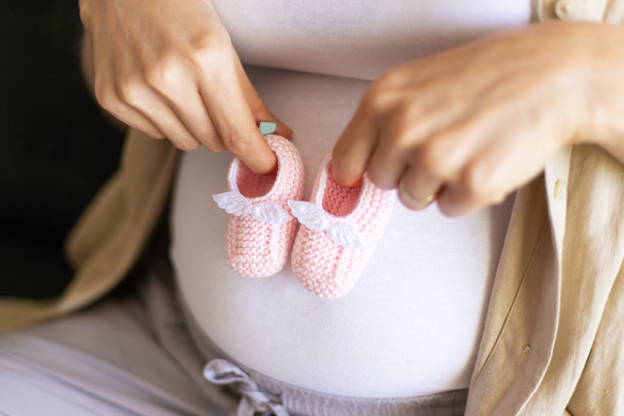 Des chaussons de bébé devant le ventre d'une femme enceinte.