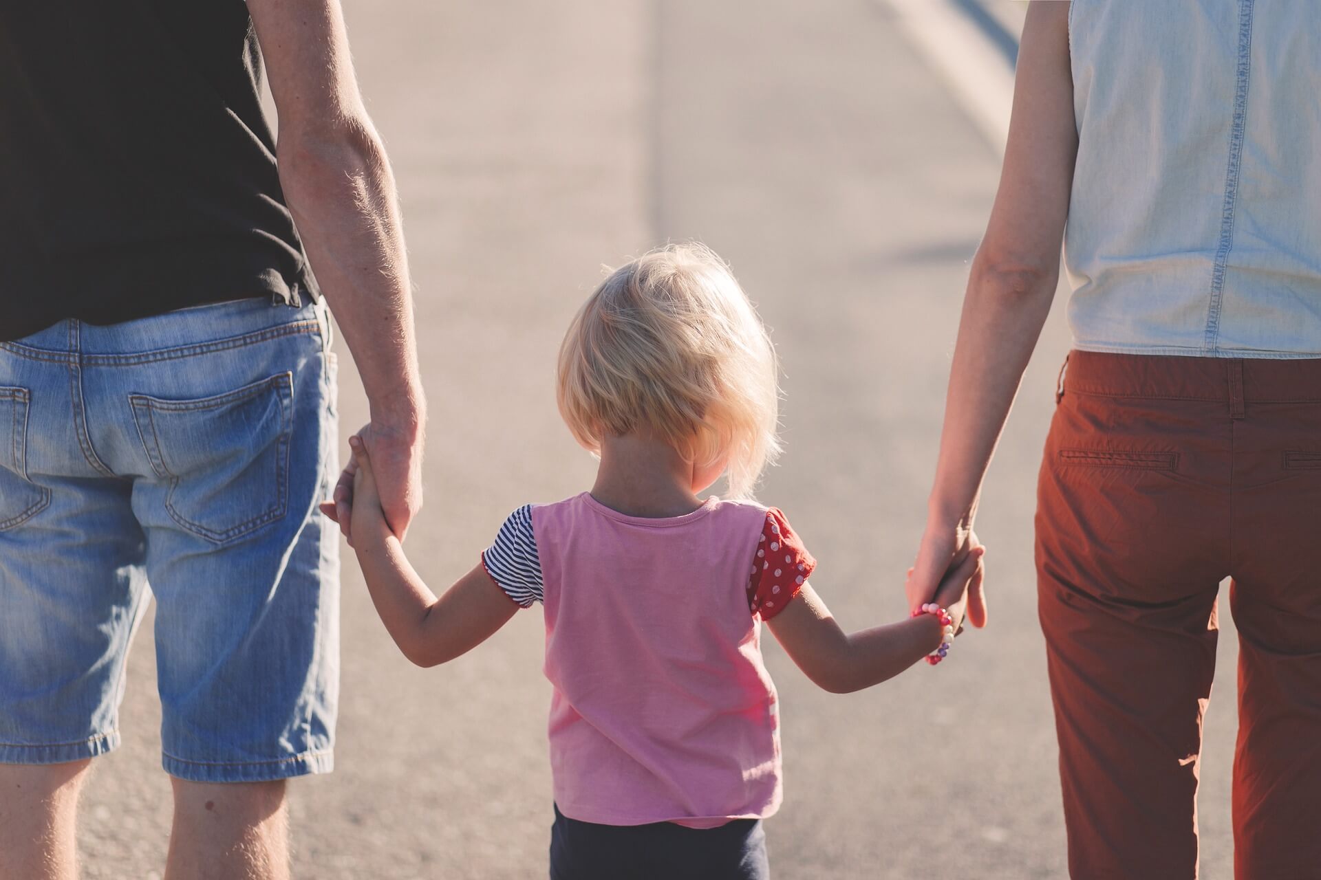 A toddler walking while holding onto her parents hands.