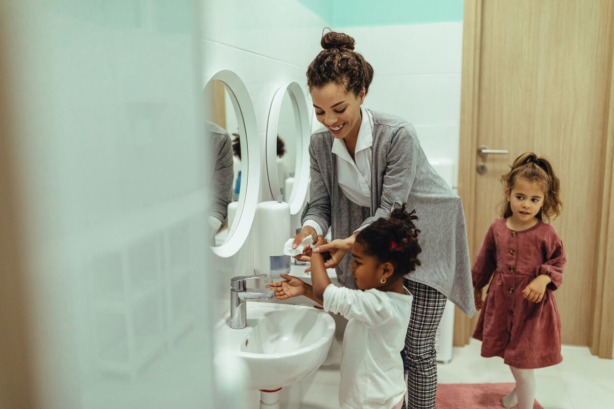 enseignante de maternelle lave les mains des filles dans la salle de bain