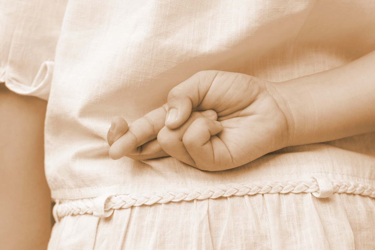 Une main d'enfant qui croise les doigts derrière le dos.