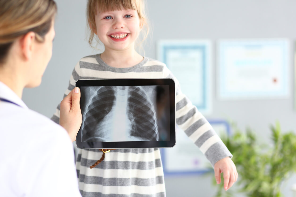 nena sonrie doctora sostiene tableta con radiografia de torax