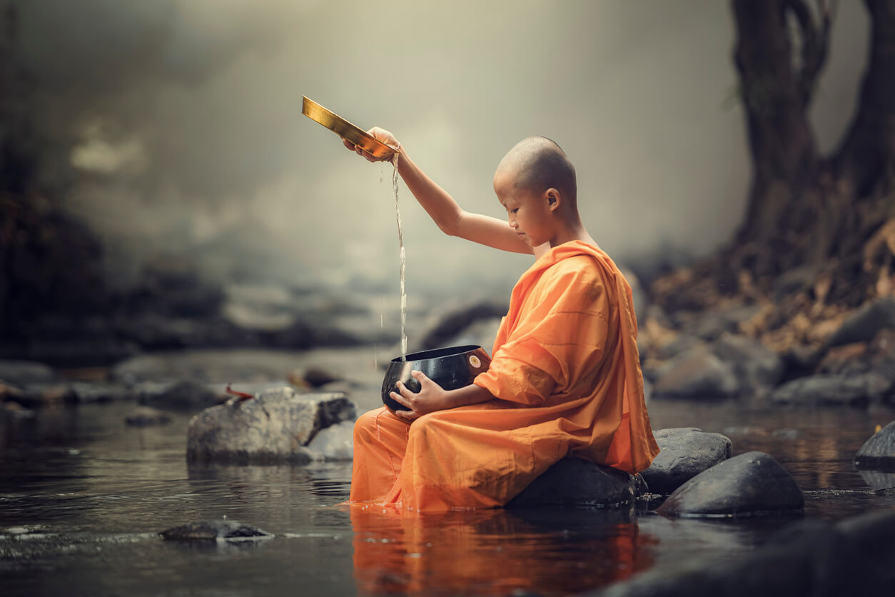Pequeno monge budista no rio mexendo com a água