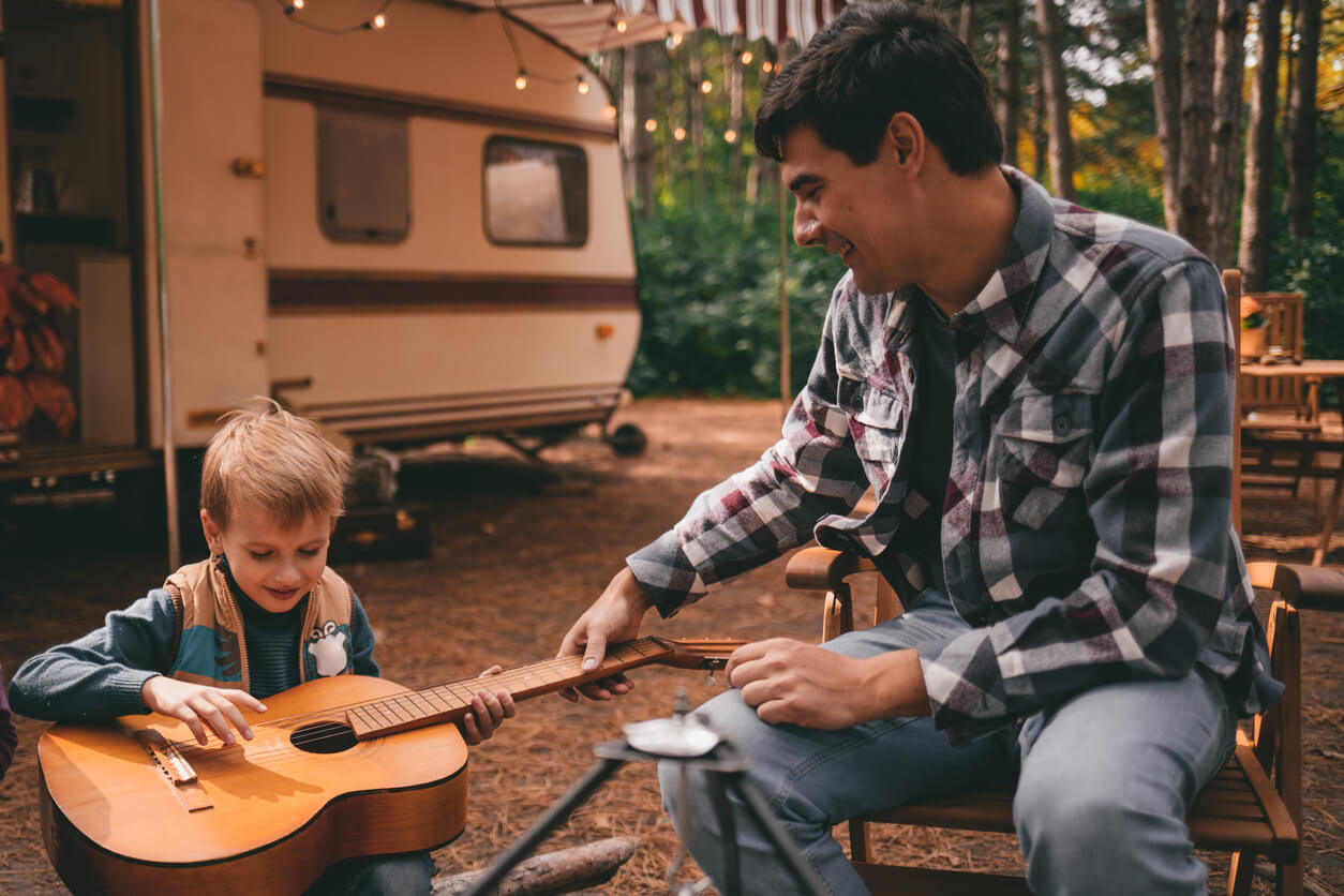 padre e hijo en el bosque tocan la guitarra camping caravana casa rodante vacaciones