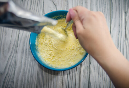 mano de madre prepara papilla de cereales industrial con leche y revuelve cuchara bol