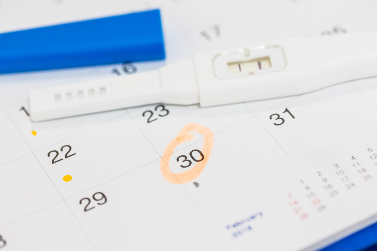 A positive pregnancy test sitting on a calendar.