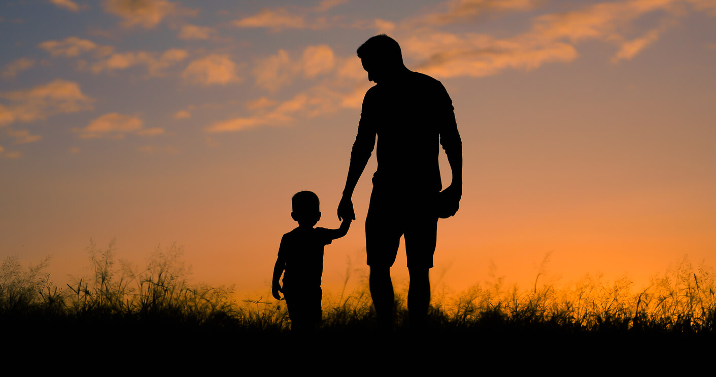 A father and son walking in a field at sunset.