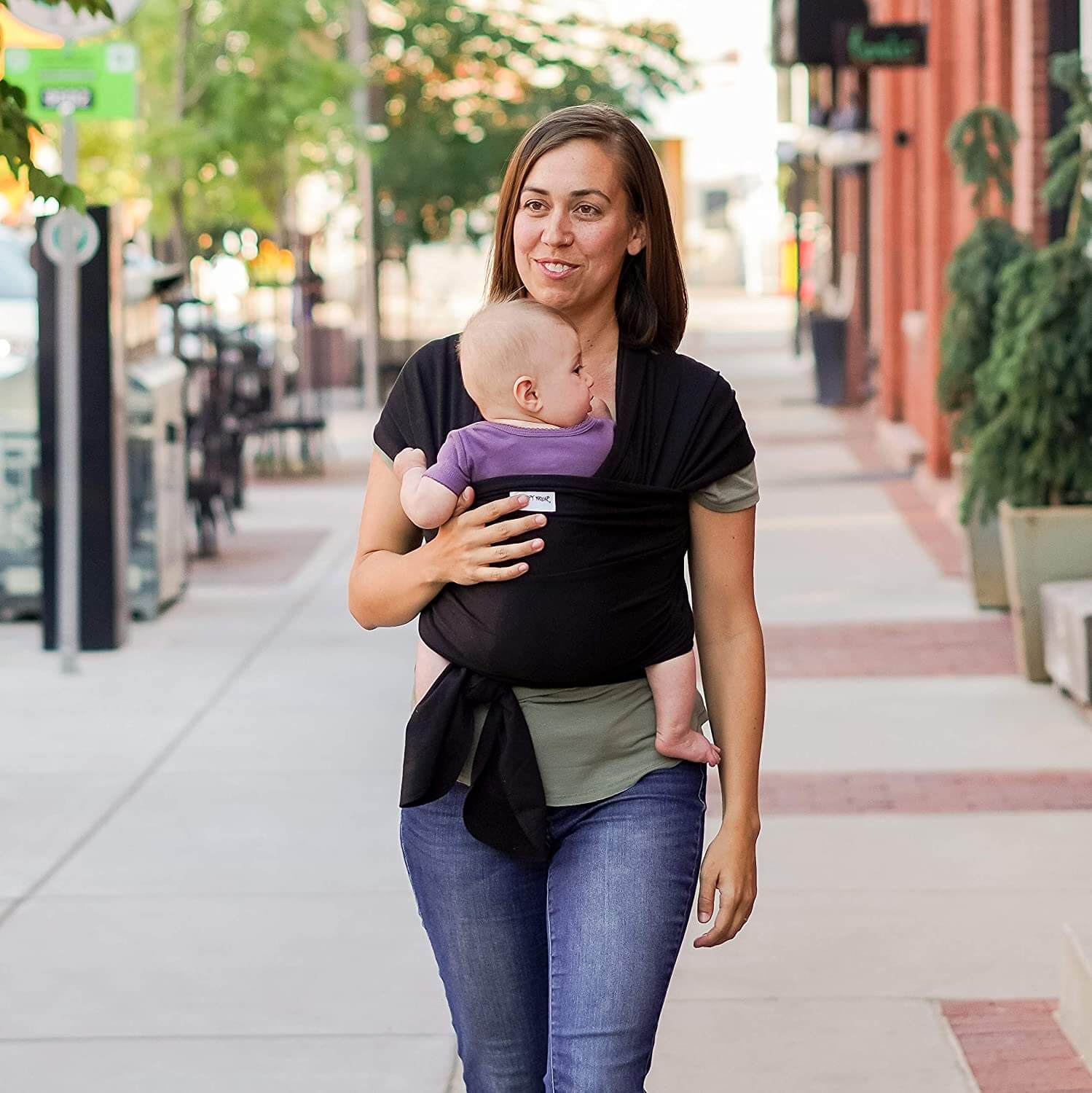 A mother walking down a city street with her baby in a baby carrier.