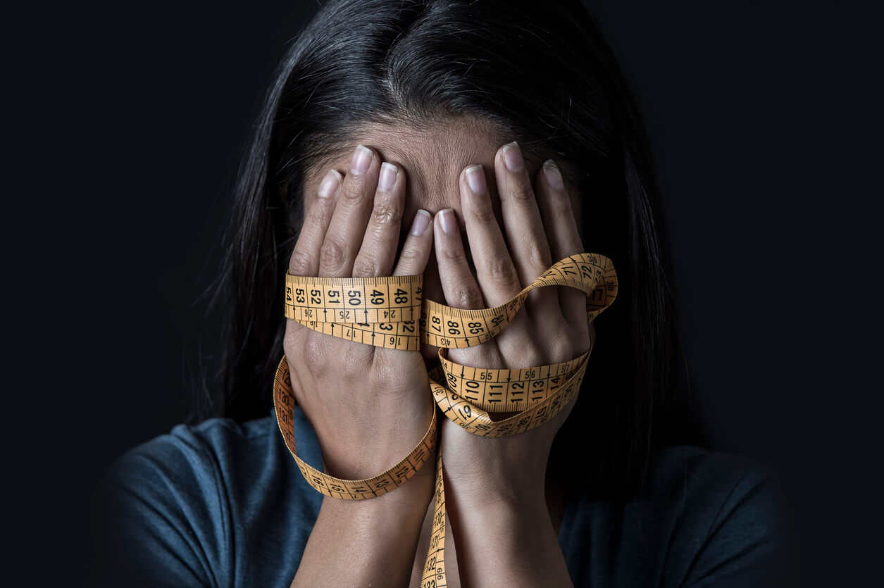A woman crying into her hands, which are bound by measuring tape.