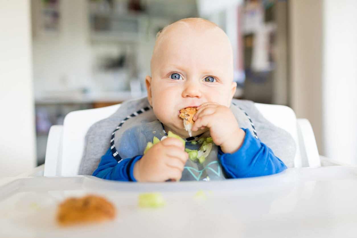 A baby eating with his hands in a high chair.