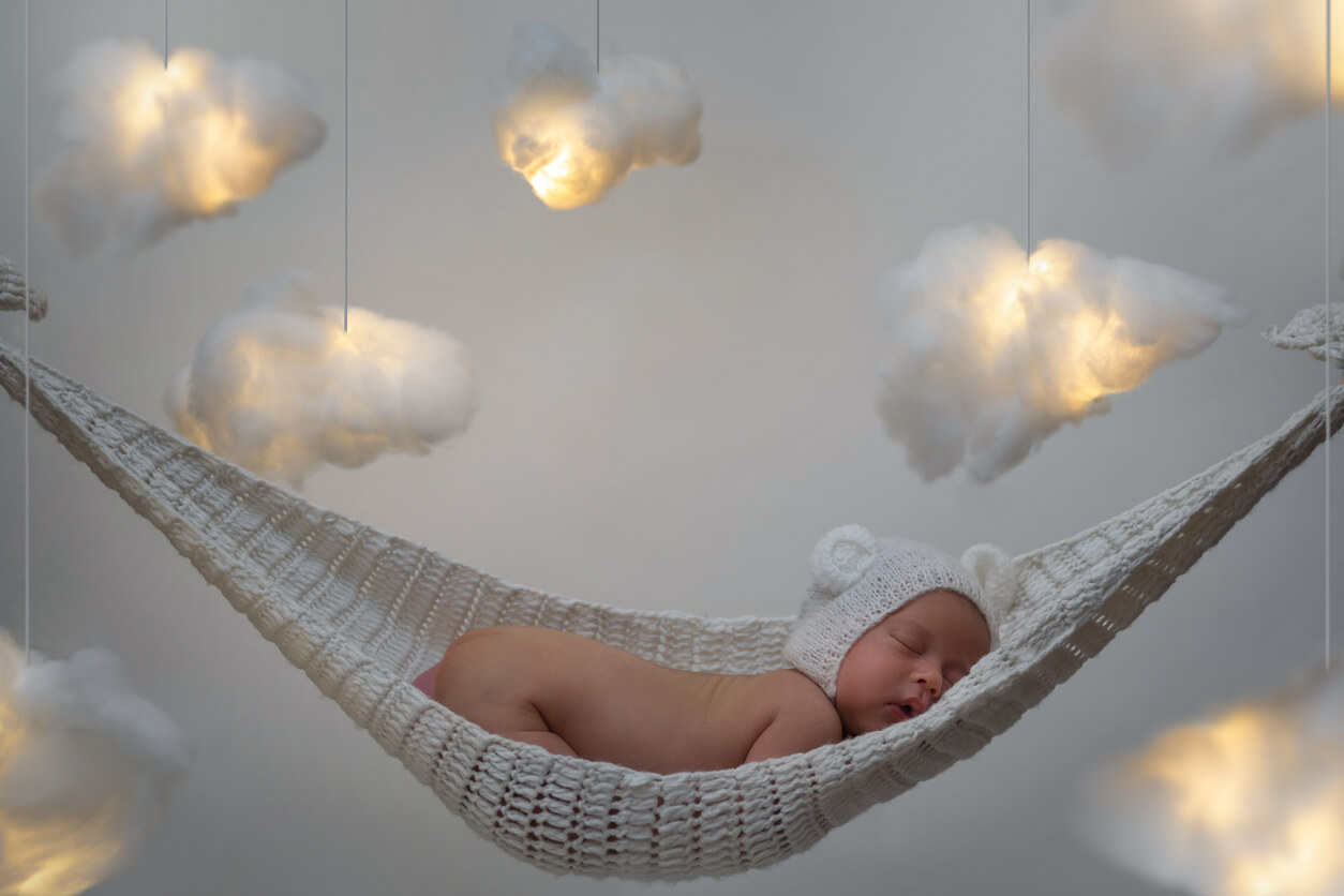 A baby sleeping on a crochet hammock surrounding by floating cotton clouds.