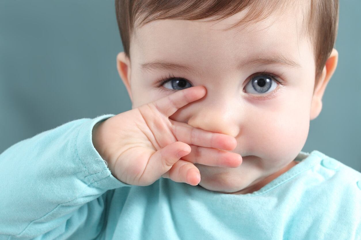 A baby wiping his nose with his hand.