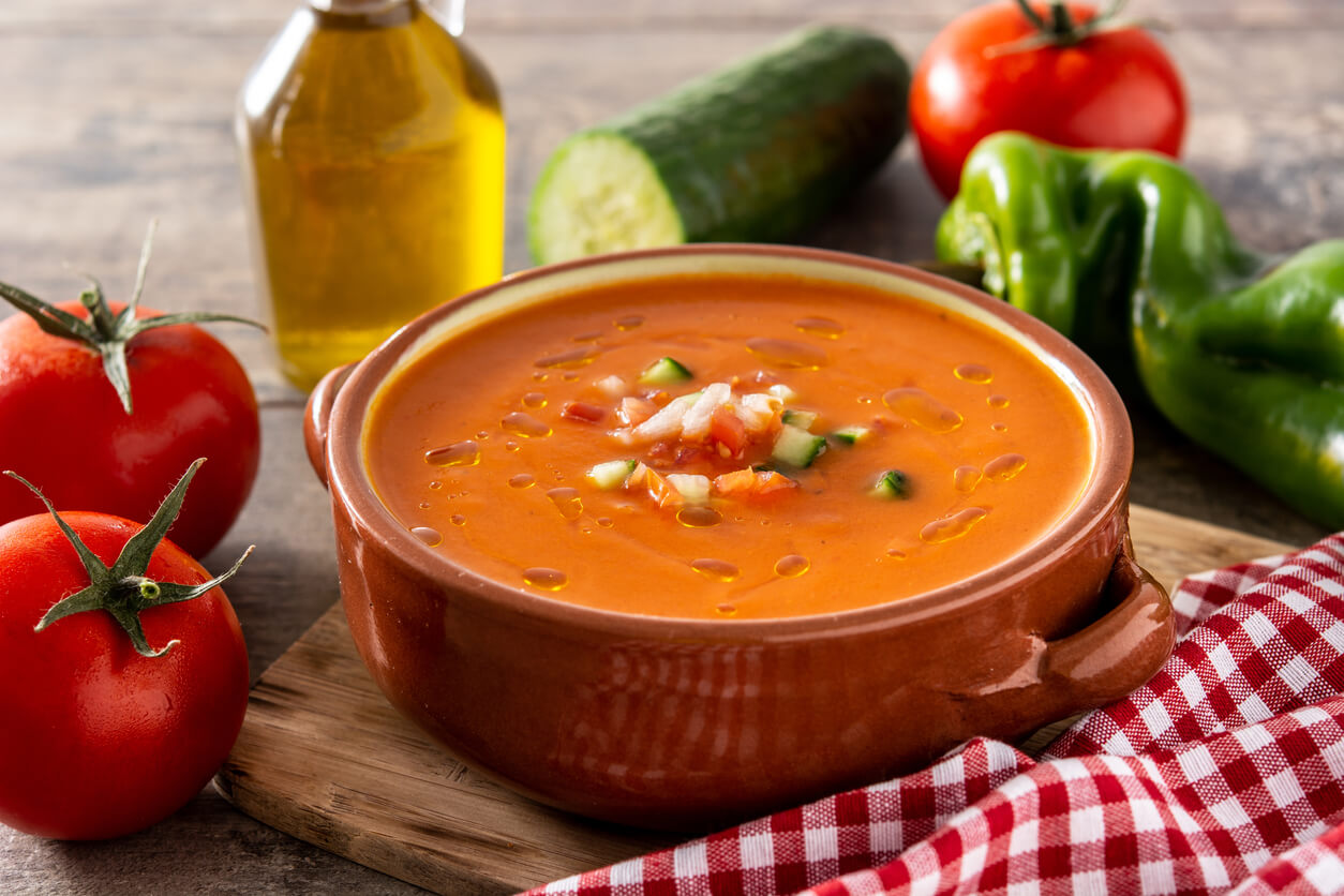 A bowl of gazpacho surrounded by fresh ingredients.