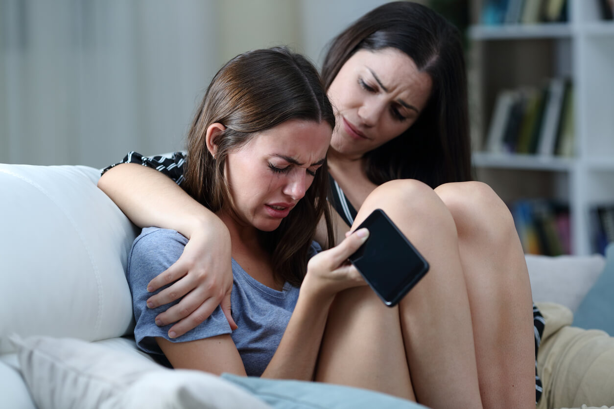mujer consuela a joven adolescente angustiada triste por acoso celular redes sociales ciberacoso