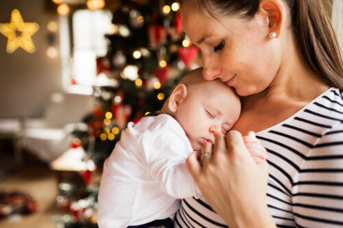 mama abraza alza a su bebe frente al arbol de navidad