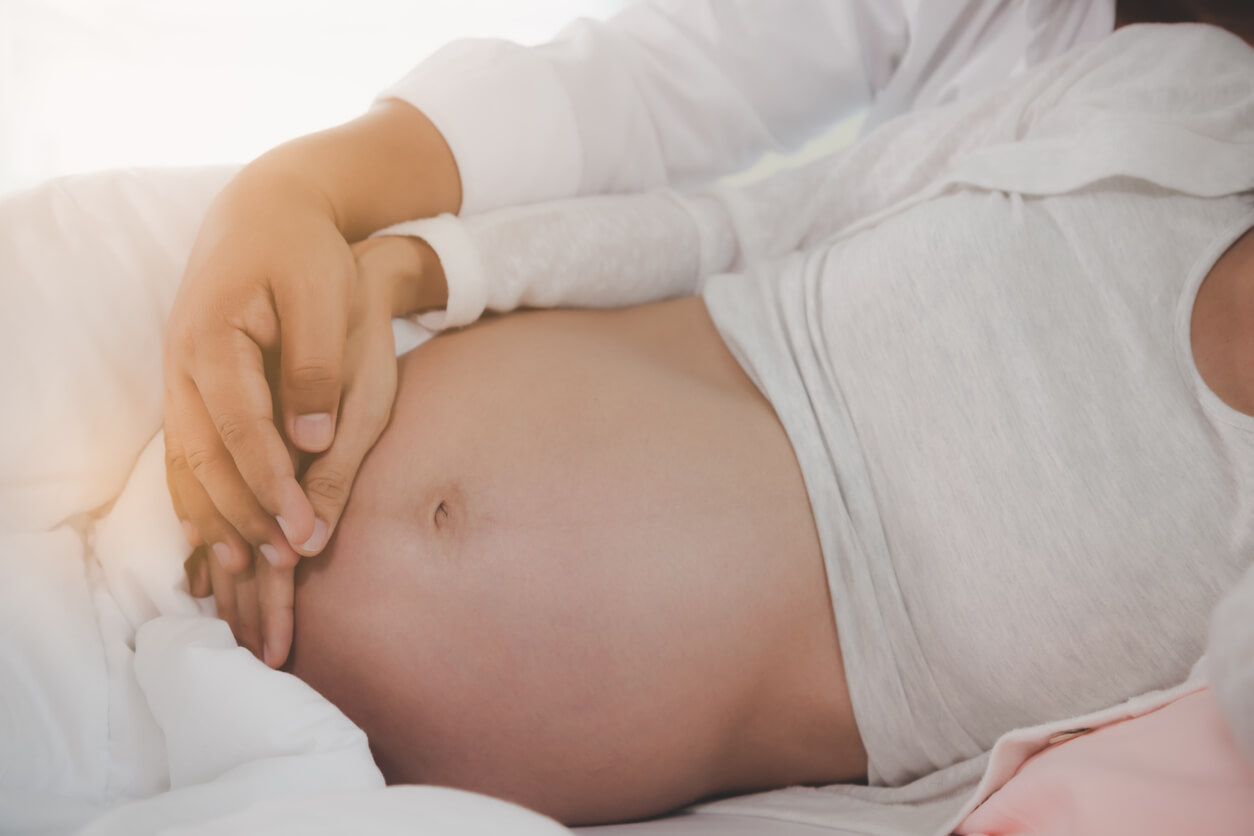Une femme enceinte allongée avec son partenaire qui écoutent les mouvements du foetus. 