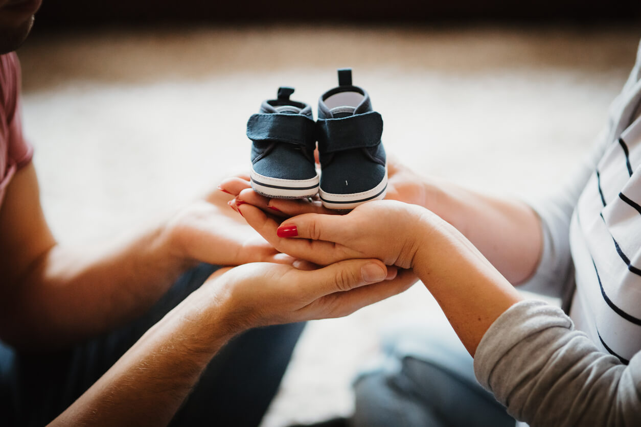 Parents holding a pair of blue baby shoes in their hands.