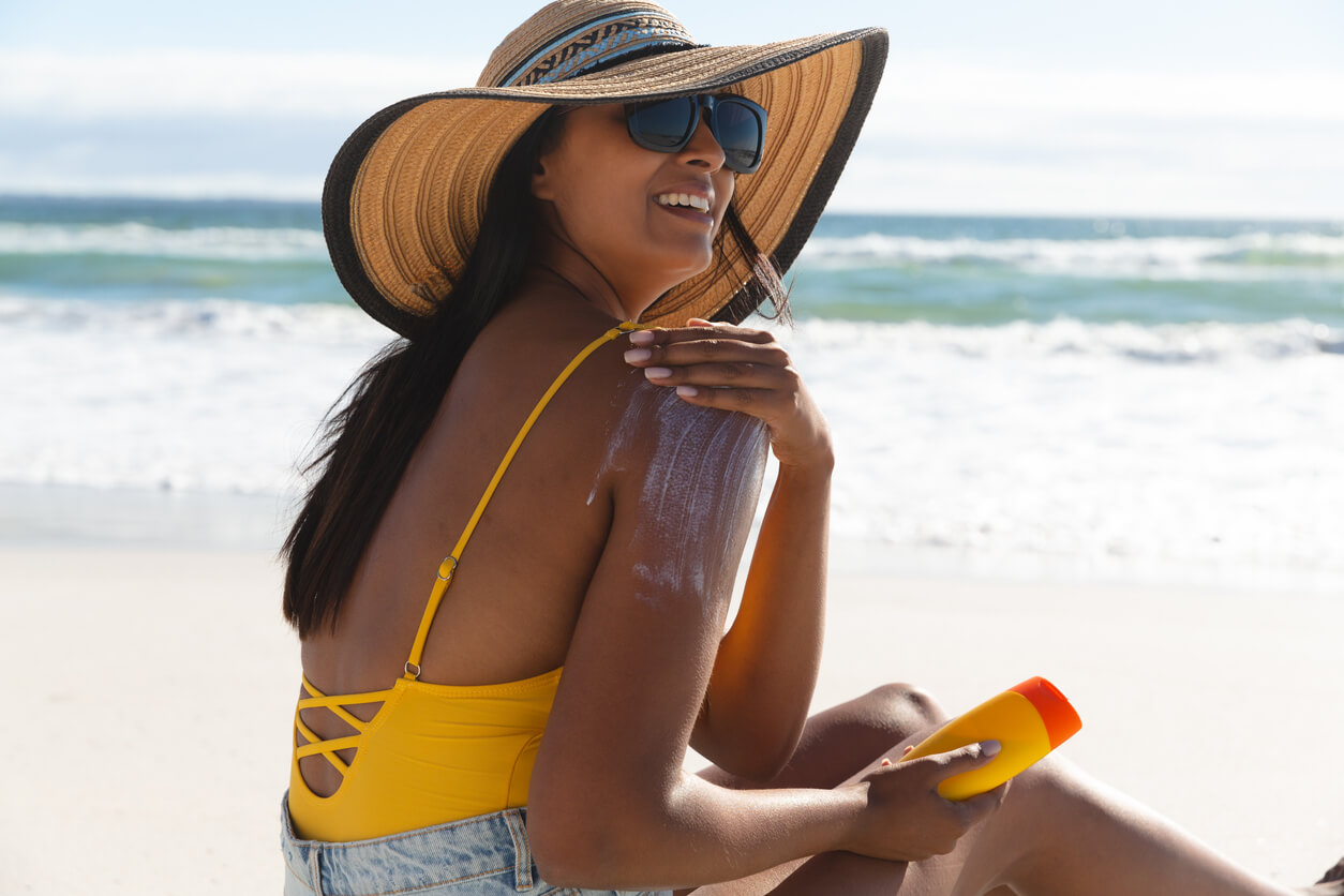 Une jeune femme qui s'applique de la crème solaire sur la plage.