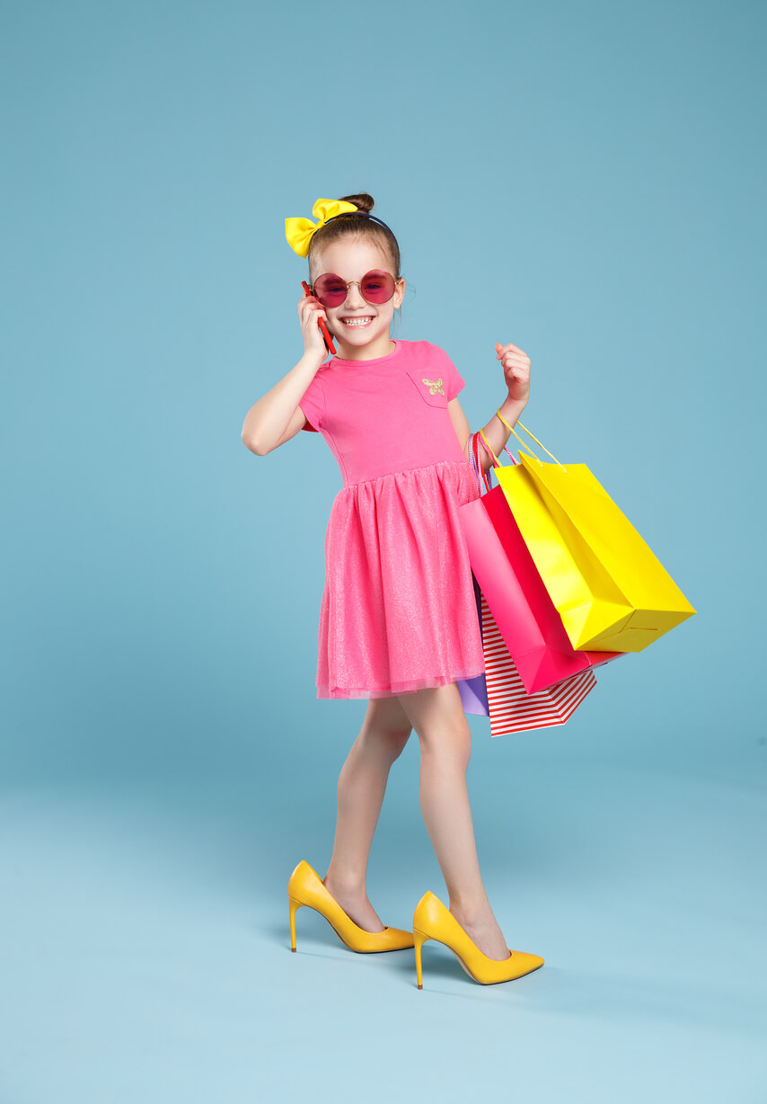 nina simula ser grande con vestido tacones bolsas bolso movil y lentes de sol