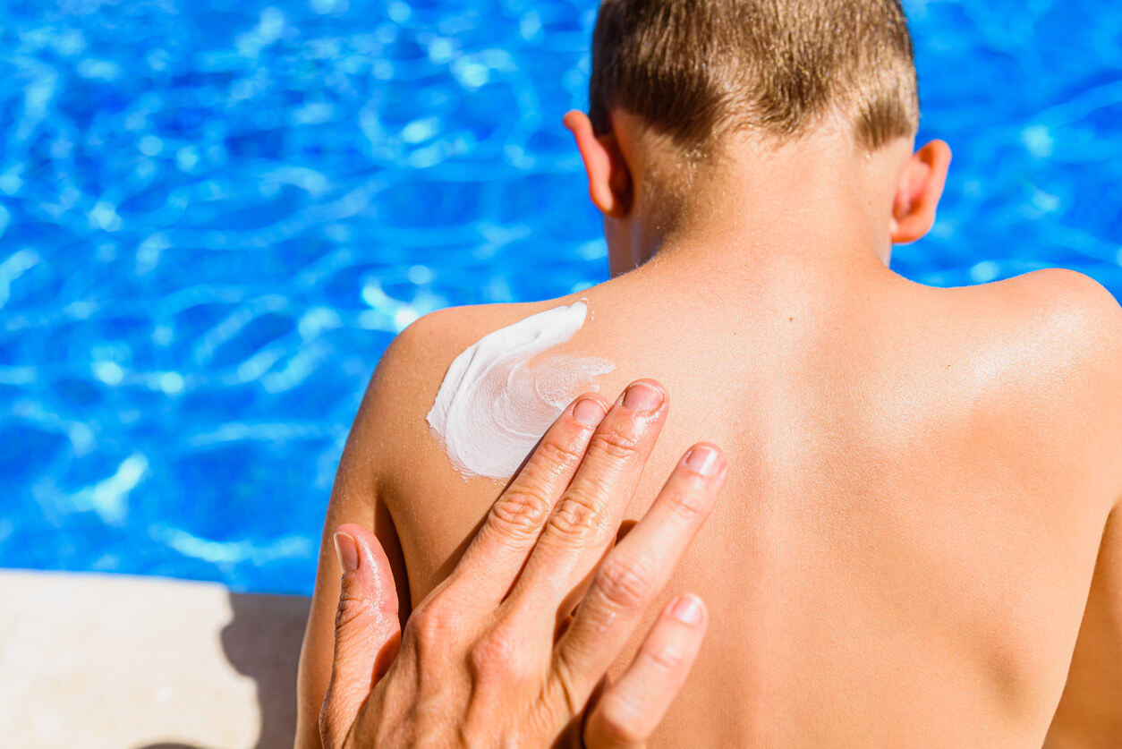 A woman rubbing sunscreen on her son't back at the pool.