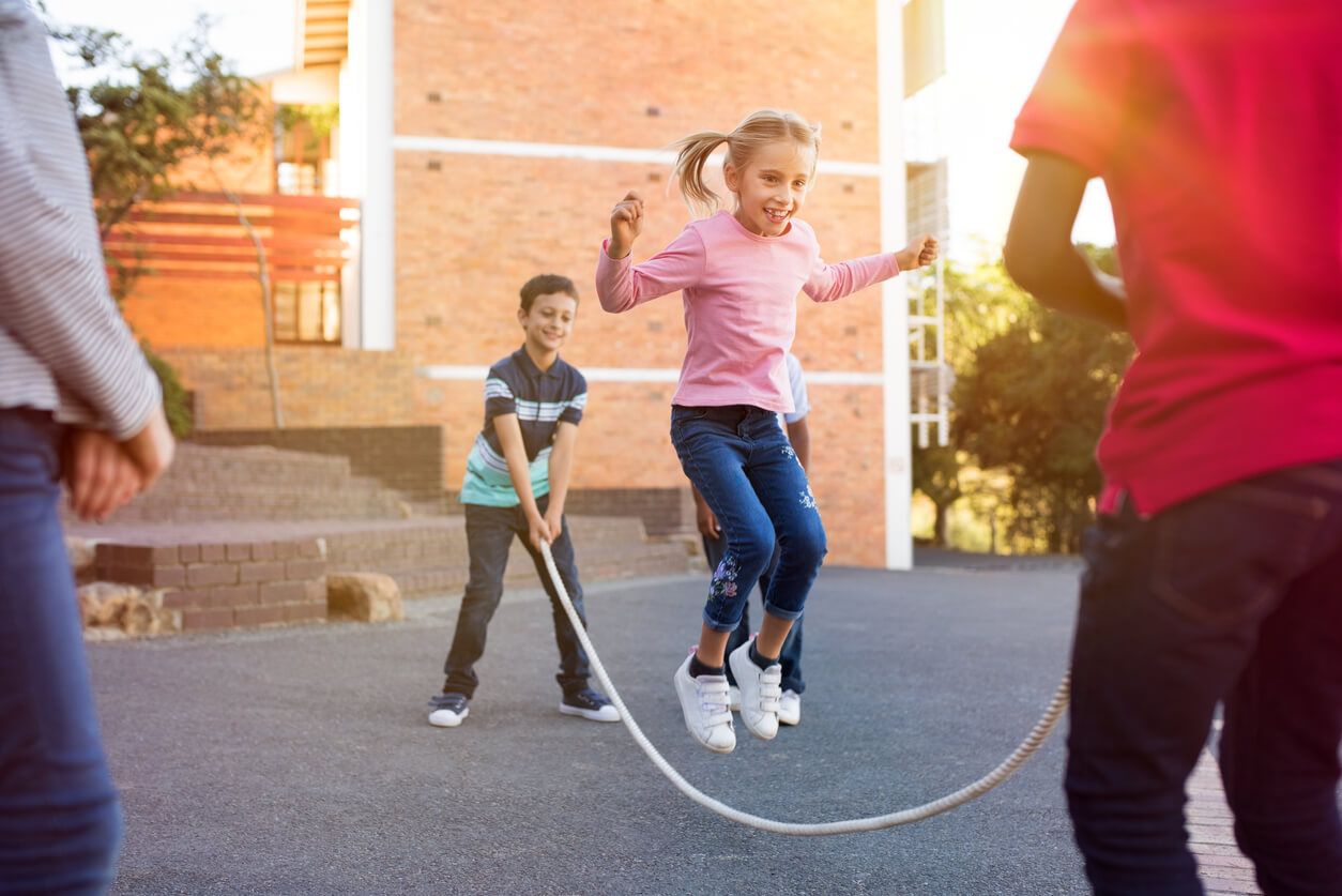 Menina e meninos pulando corda no pátio da escola