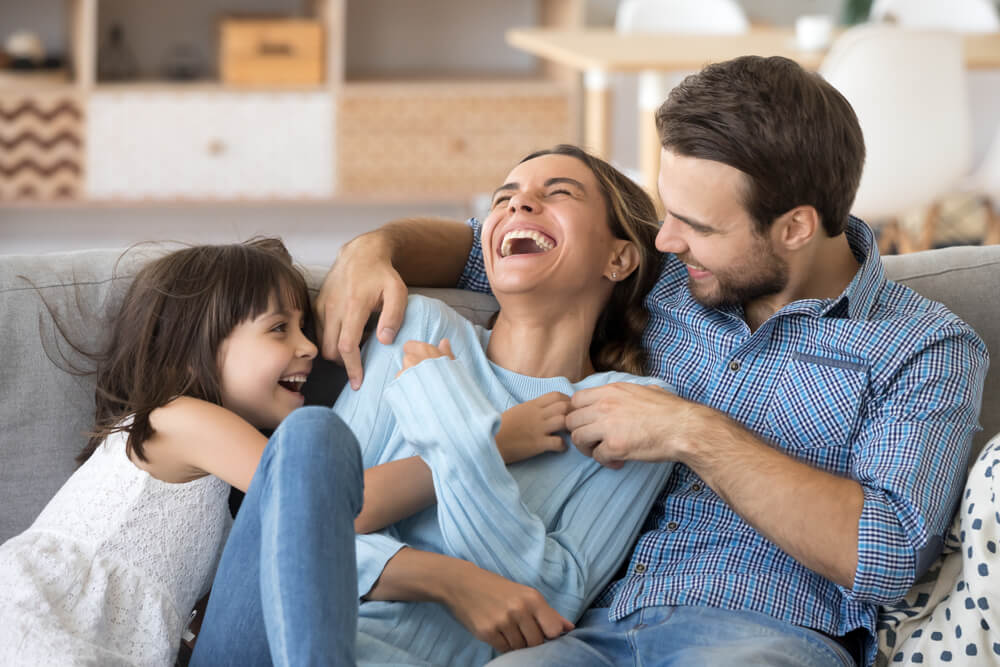 A girl laughing with her parents on the couch.