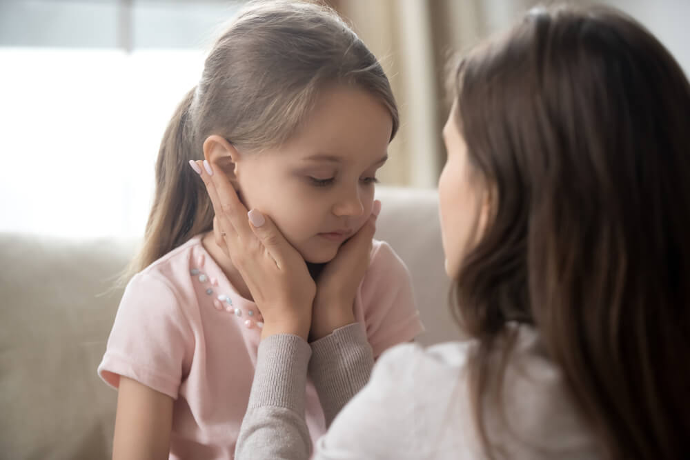 A little girl looking ashamed while talking with her mother.