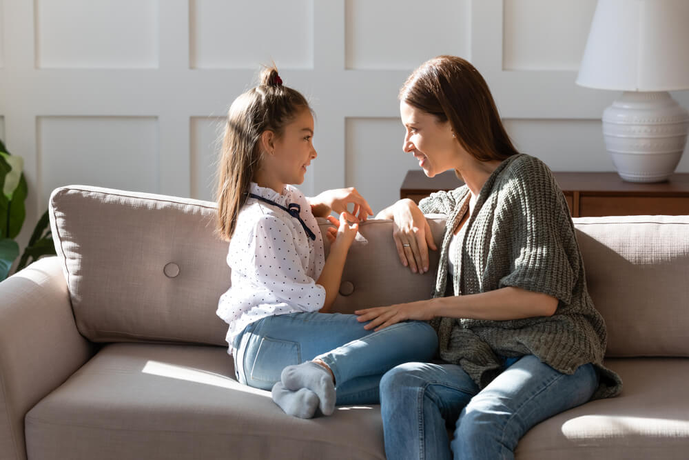 A girl and her mom having a relaxed conversation on the couch.