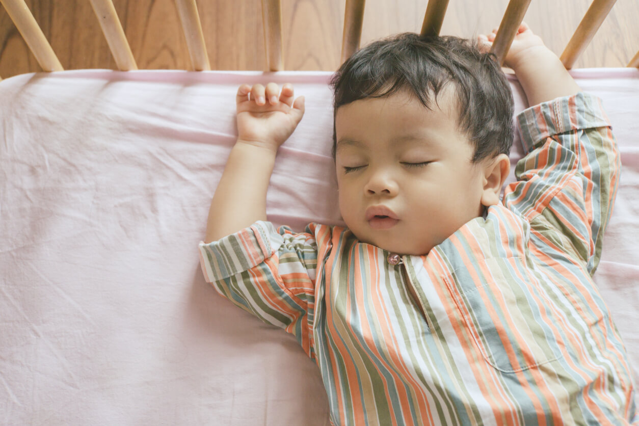 Un bébé allongé sur le dos dans un lit à barreaux.