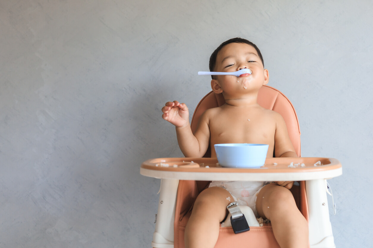 A toddler feeding himself in his highchair.