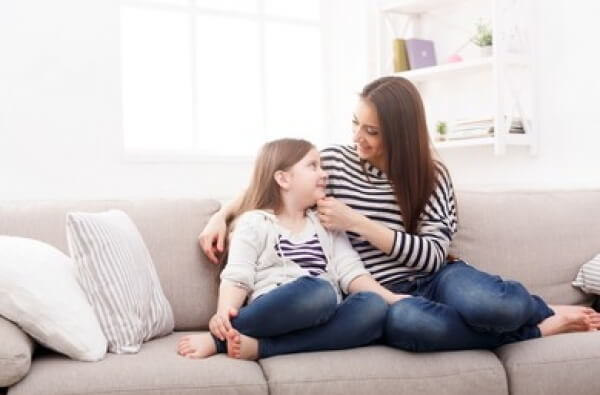 Äiti ja tytär istuvat sohvalla keskustelemassa luottamuksellisesti ja kunnioittavasti.