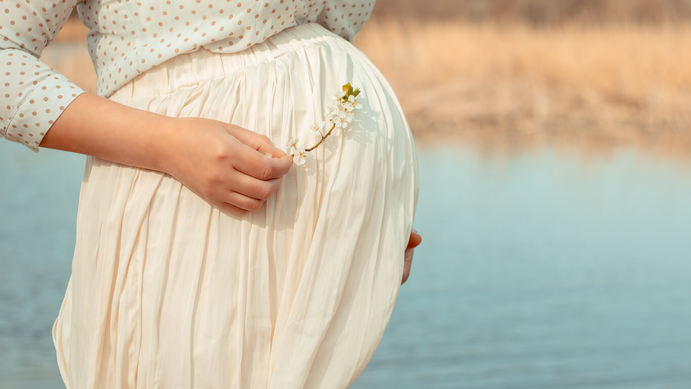 A pregnant woman standing by a lake.
