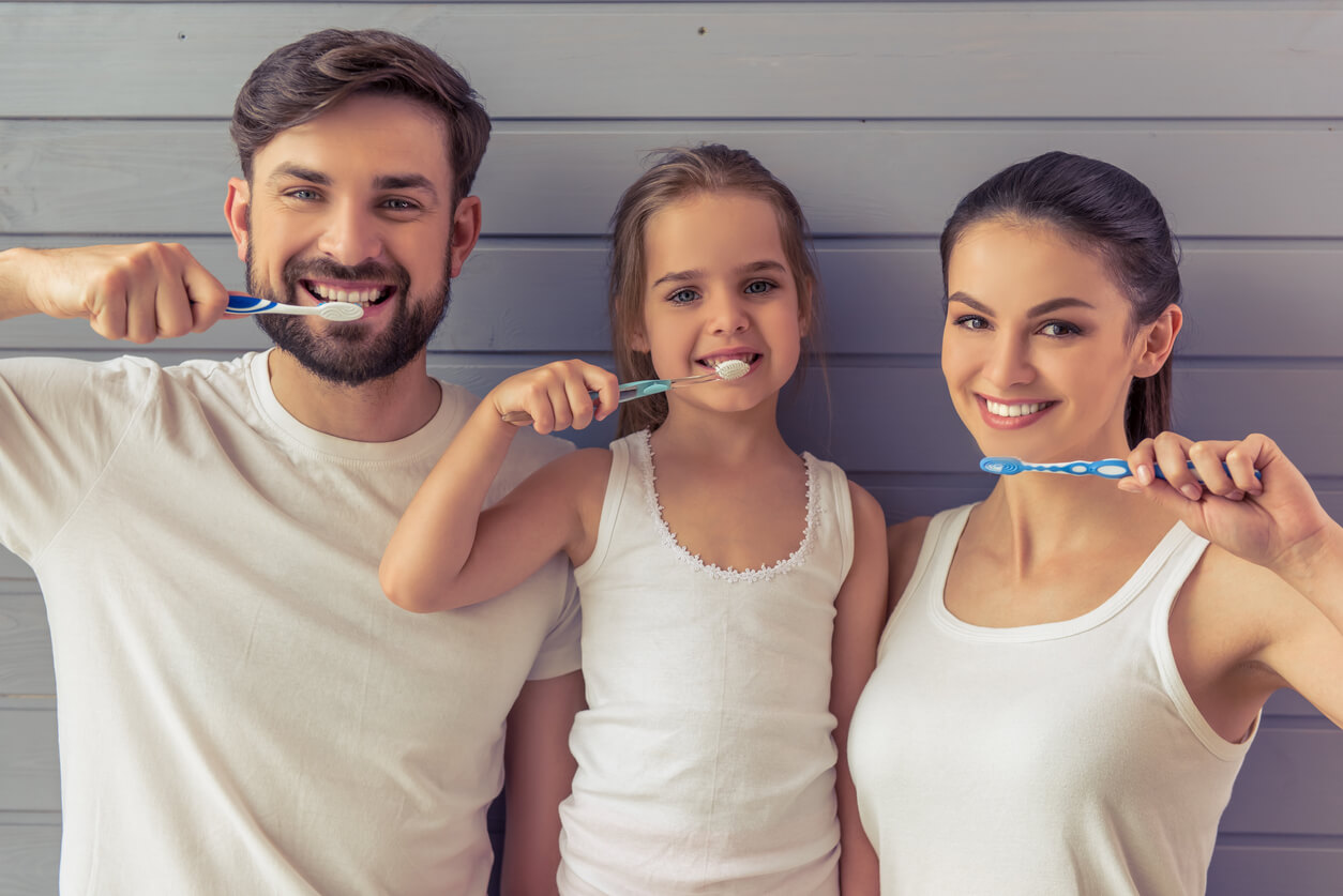 A mother, father, and daughter brushing their teeth.