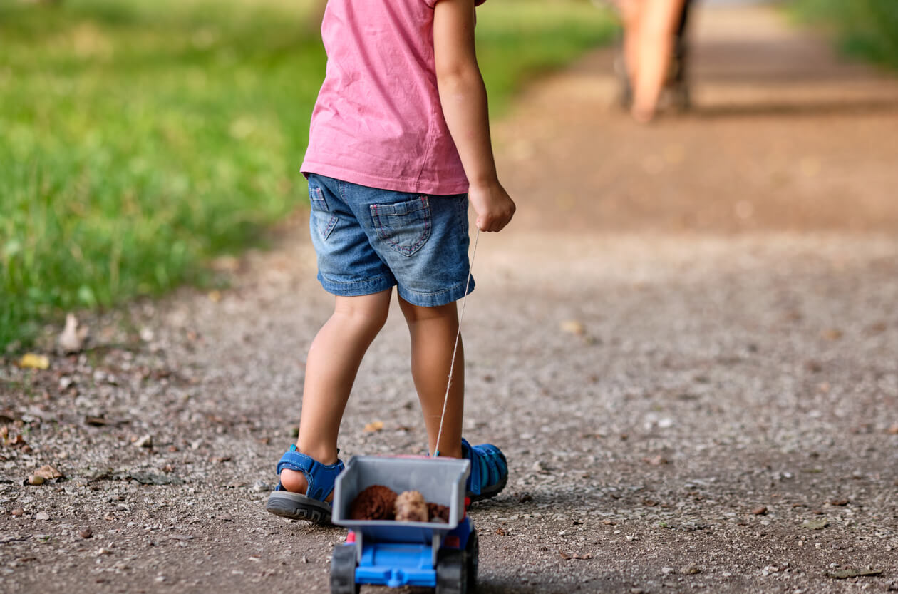 Et tre år gammelt barn som drar en lekebil nedover en grussti.