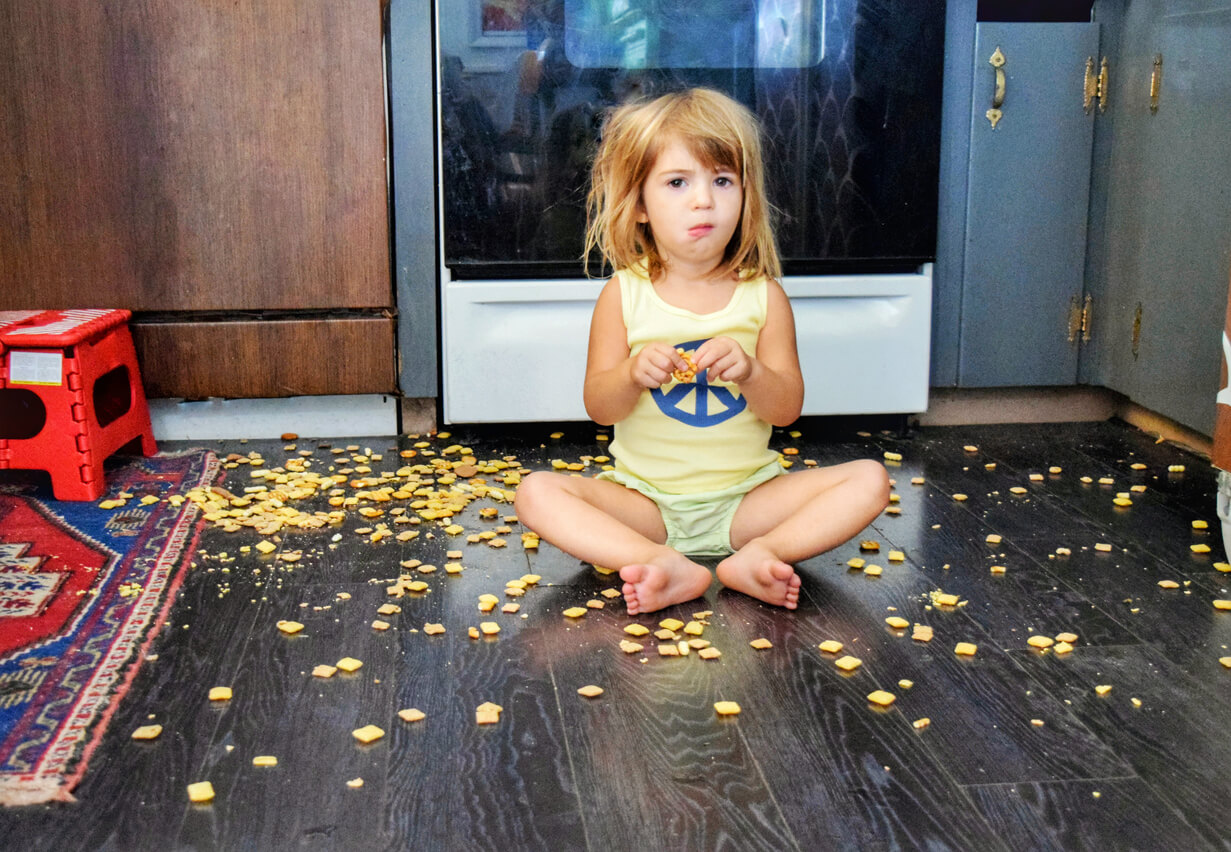 A toddler sitting on the floor in the middle of a pile of crackers.