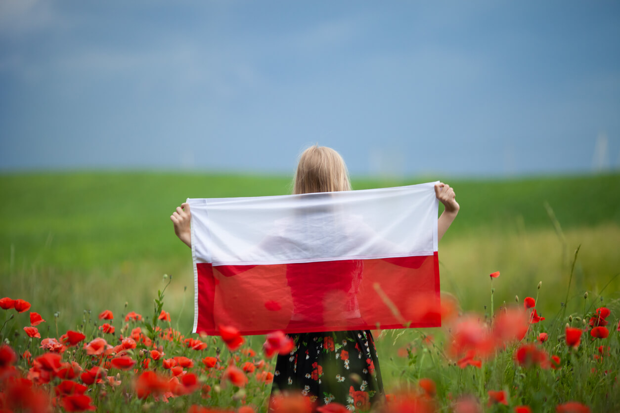 A blond girl standing in a poppy field holding a Polish flag.
