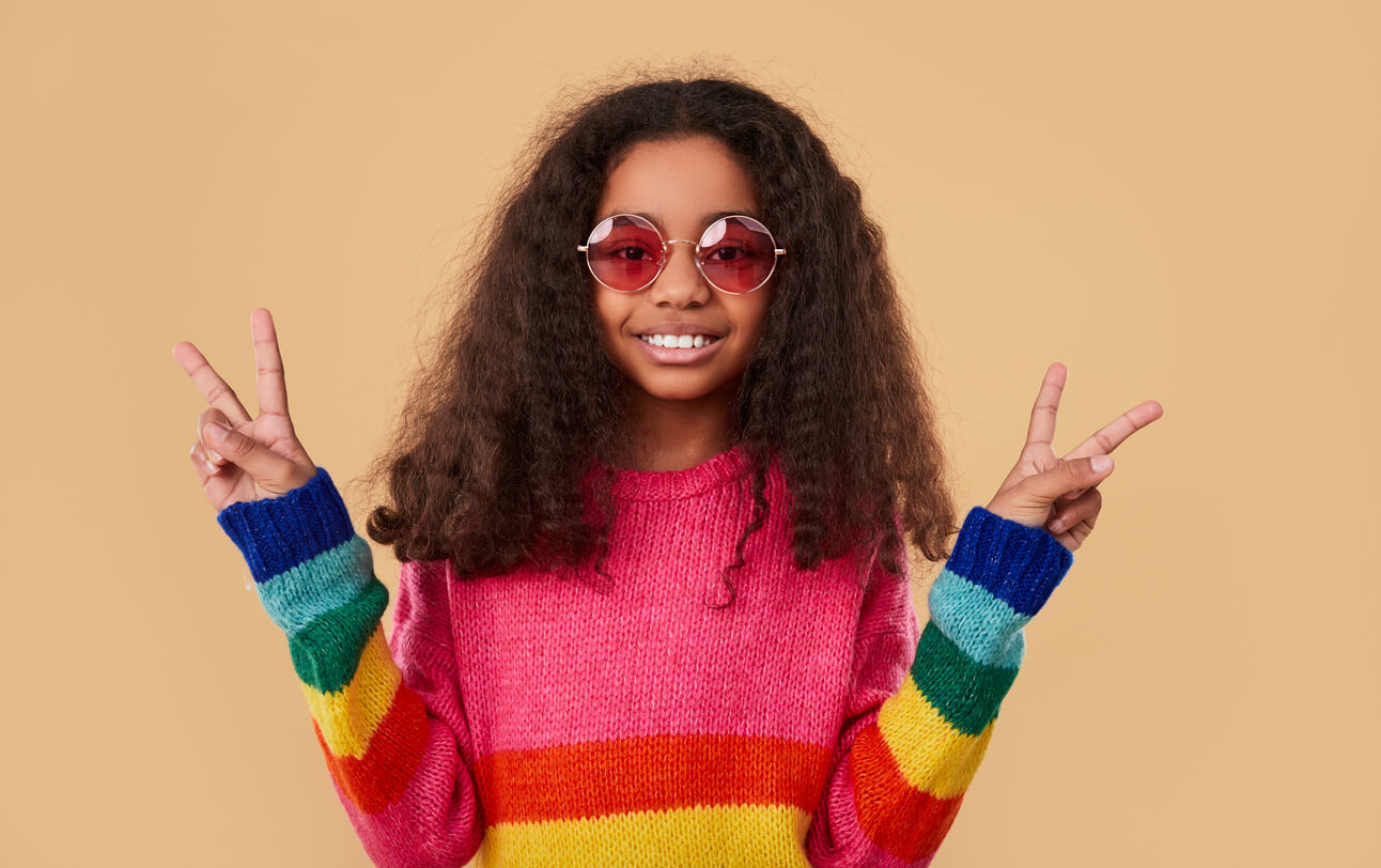 nina afroamericana con abrigo colorido hippie simbolo paz con los dedos de las manos