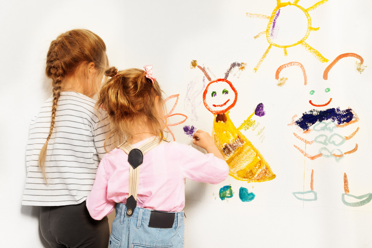 Two small girls painting on the wall.