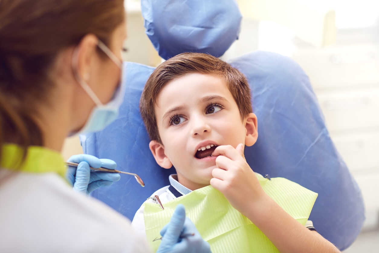 ragazzo seduto sulla poltrona del dentista mostra il suo dente