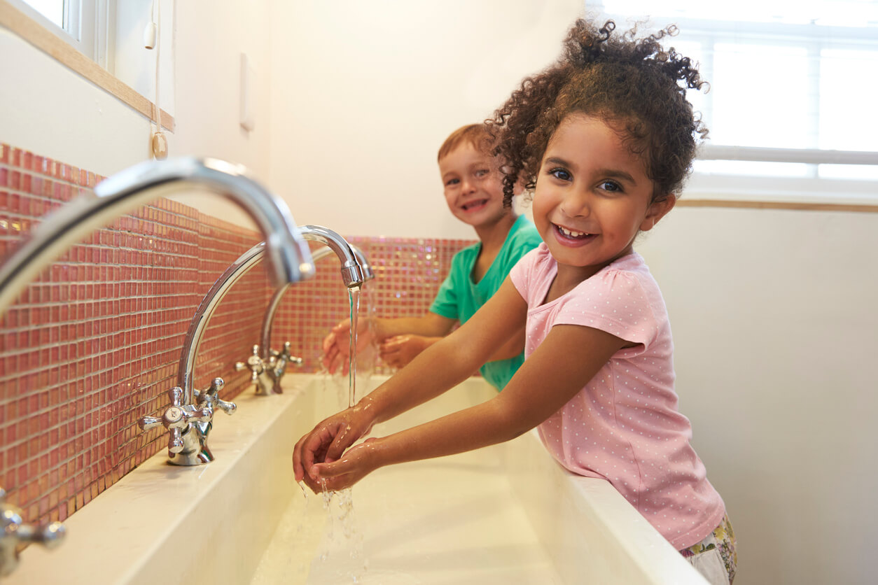 ninos pequenos se lavan las manos con agua y jabon en lavatorio del bano del jardin
