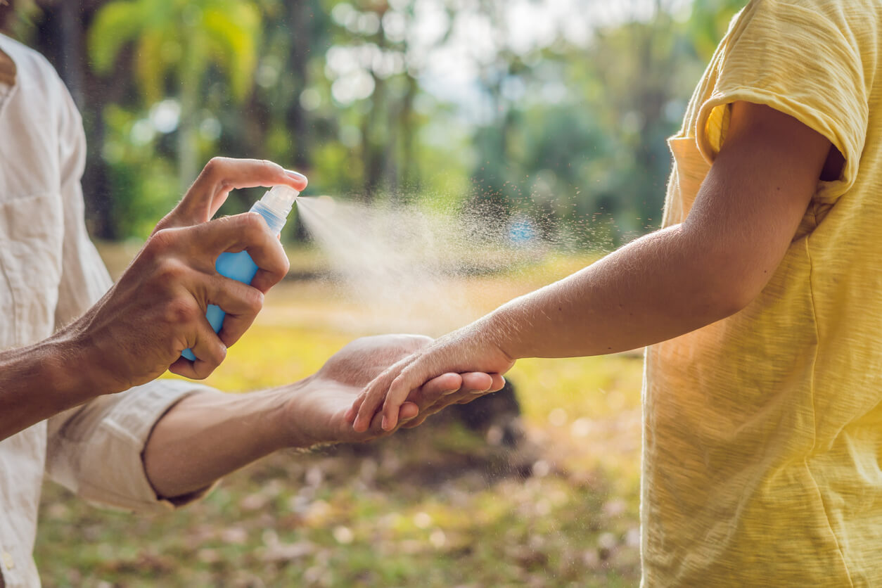 Un adulte qui spray le bras d'un enfant avec de l'antimoustique.